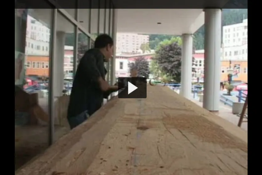 A screenshot from the video of a carver using traditional tools to shape a canoe.