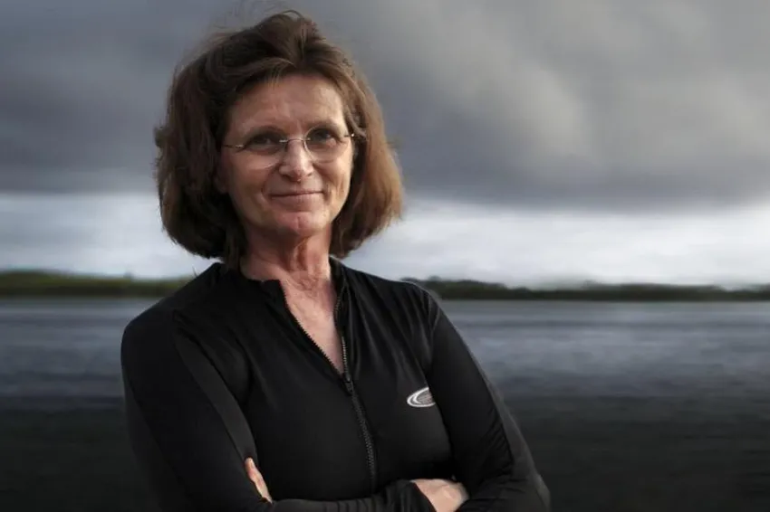 Nancy Knowlton stands with her arms crossed in front of the ocean. 