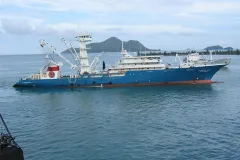 A large blue and red fishing vessel sits on the water. 