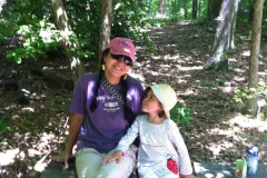 a young mother in colorful hiking attire sits on a bench with her young daughter
