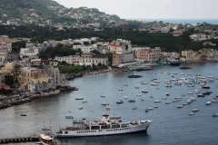 A photo of a seaside town with boats docked in the harbor and buildings along the shore. 