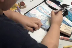A student uses a marker to decorate a reusable lunch bag with ocean creatures