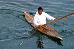 a man in a white hooded sweatshirt paddles in a skin boat kayak