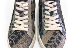 A pair of silver colored sneakers with white shoelaces, made from fish skin and dyed with blue floral patterns.