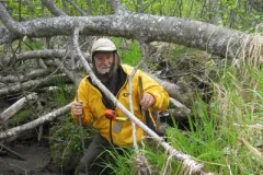 Botanist Dennis Whigham stands in a forested wetland with field gear. 