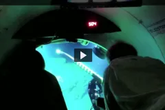 Screenshot from "Deep Reef Observation Project Video" showing two researchers looking out a window of a submersible.