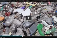 A screenshot from the video showing trash on a rocky beach. 
