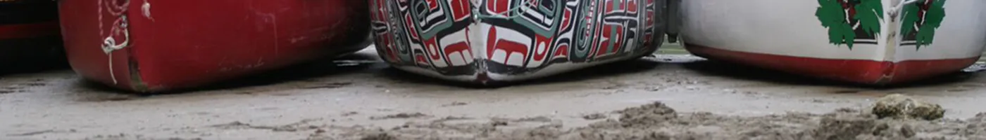 Canoe hulls on a sandy shore are painted with traditional Alaskan figures.
