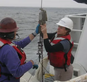 Dr. Karen Osborn wearing a hard hat and working with equipment on a ship.