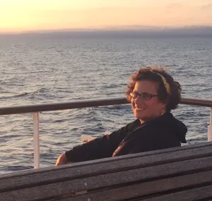 Karen Romano Young sitting on a bench with a sunset in the background.