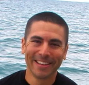 Andrew Altieri smiling at the camera in a headshot with water in the background.