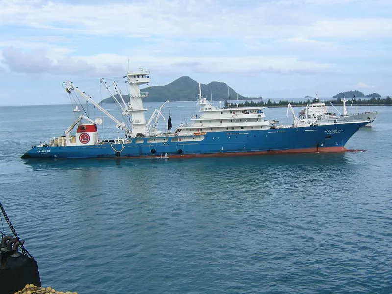A large blue and red fishing vessel sits on the water. 