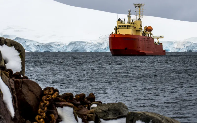 a orange and yellow ship with glaciers in the background