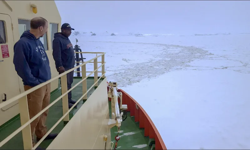 two men on the deck of a ship assessing the ice in the ocean