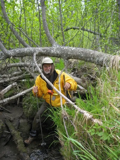 Botanist Dennis Whigham stands in a forested wetland with field gear. 