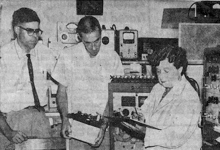 a woman with clipboard and two male assistants