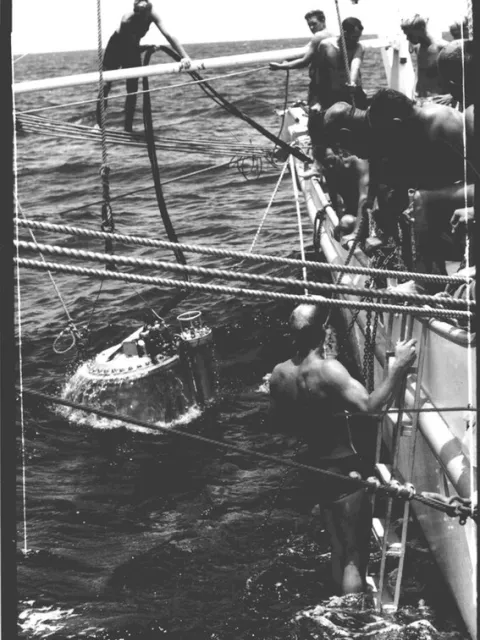 a submersible chamber sits at the ocean surface next to a ship